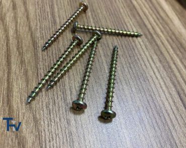 A collection of yellow zinc-plated pan head chipboard screws from THV Fasteners, scattered on a wooden surface, emphasizing their robust finish and strong hold for furniture assembly.